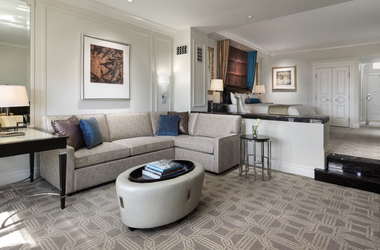 A modern living room with a gray sectional sofa, blue and brown cushions, an ottoman, and a framed artwork on the wall.