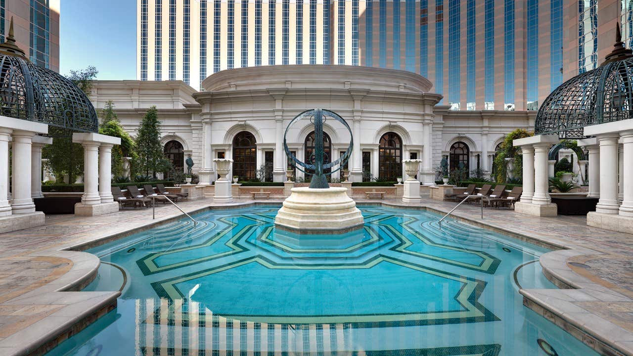 Elegant hotel pool area surrounded by columns and ornate domes, with a central statue and tall buildings in the background.