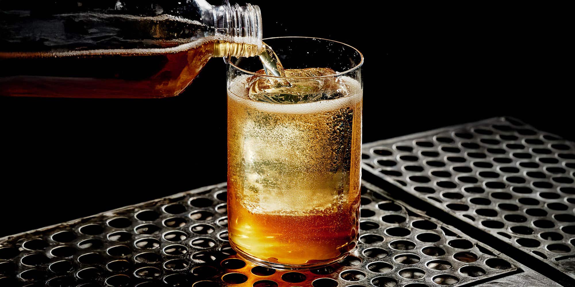 Liquid from a bottle poured into a glass with ice.