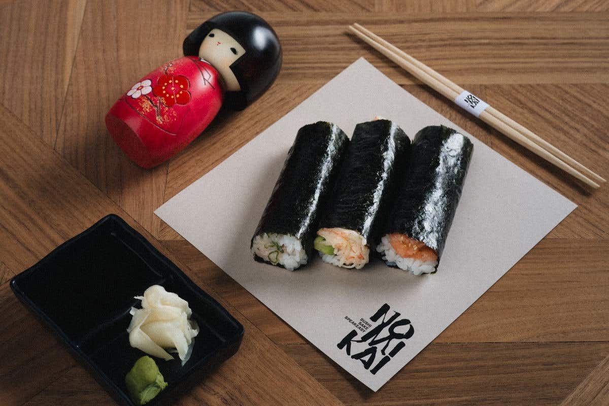 Three sushi hand rolls served with wasabi, pickled ginger, and chopsticks.