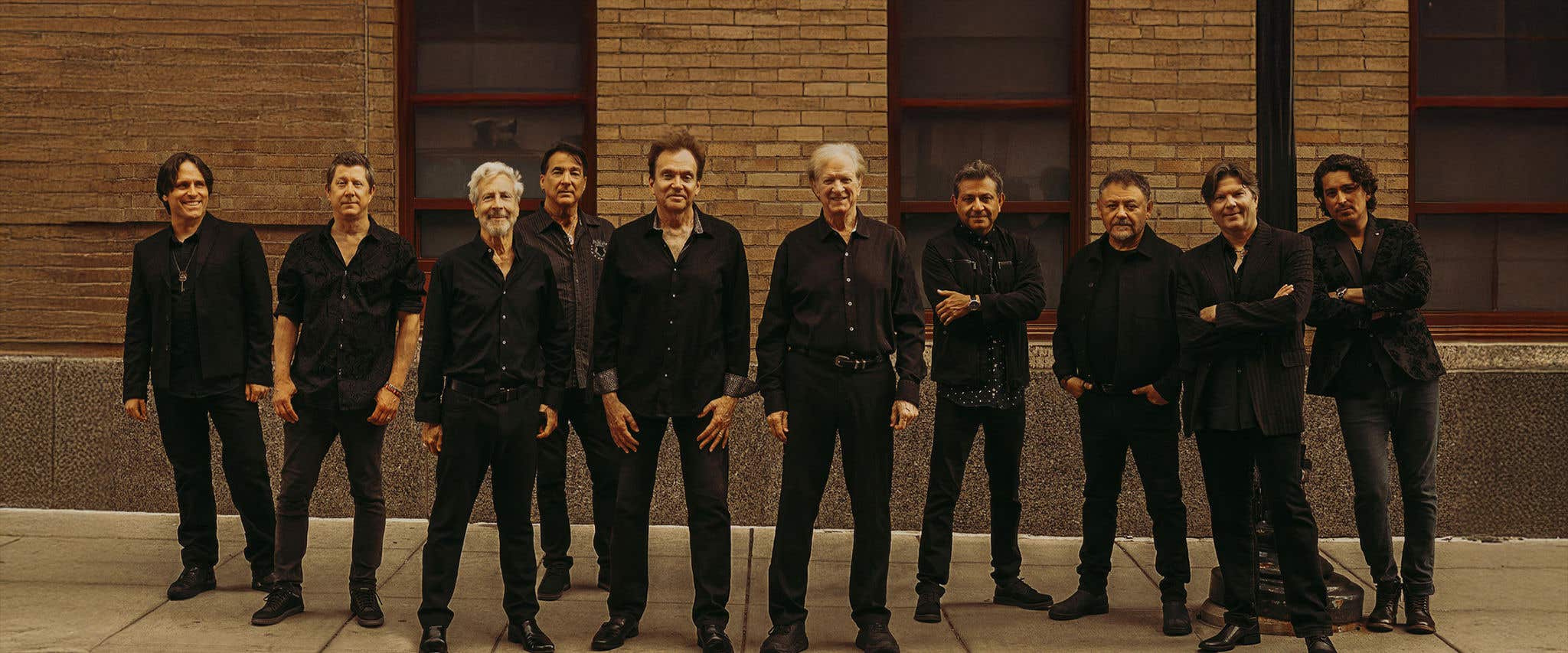 Chicago band members dressed in all black standing in front of a brick building looking at the camera.  