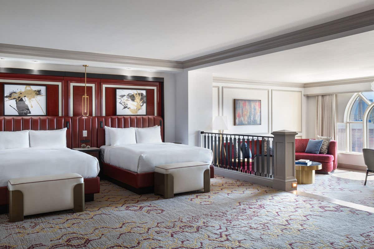 Spacious hotel room with two beds, a seating area, and large windows.