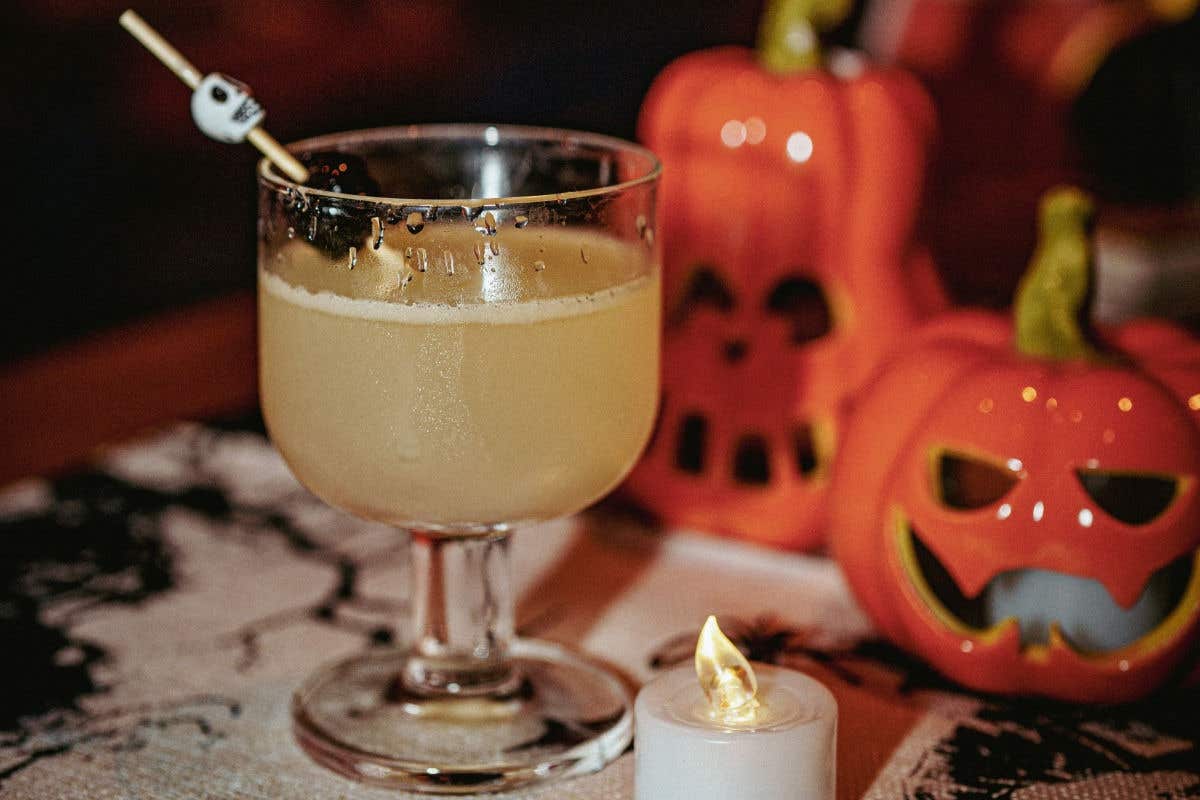 Halloween cocktail served in a stemmed glass with a skull garnish and pumpkin decorations.