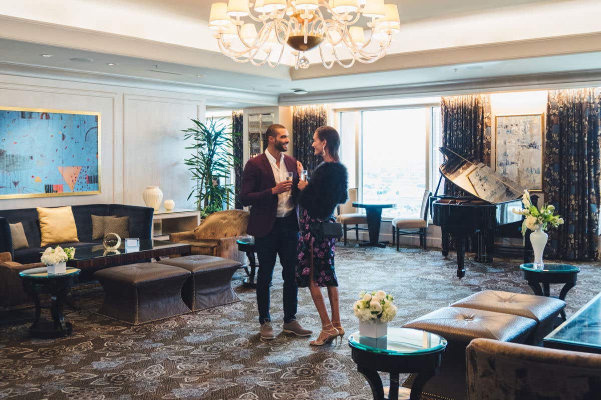 A man and woman stand with drinks talking in the middle of a luxurious club lounge.