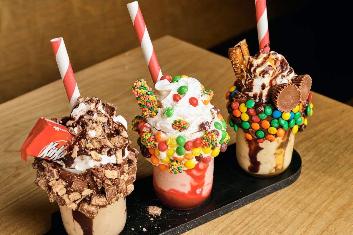 Three mini shakes each one with different candy sprinkled on top and a red and white straw. 