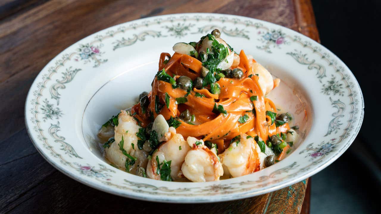 Plated silken pasta with large prawns, garlic, and capers in a light lemon butter sauce garnished with fresh parsley