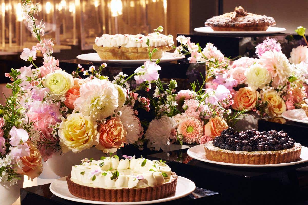 Assorted pies displayed on stands with lush pink and peach floral arrangements.
