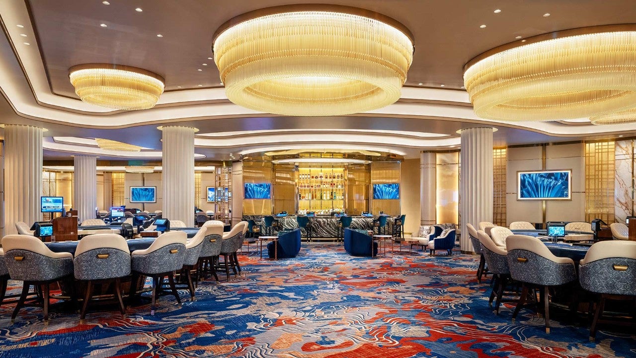 A luxurious casino lounge with a bar, gaming tables, and comfortable seating areas under elegant chandeliers.