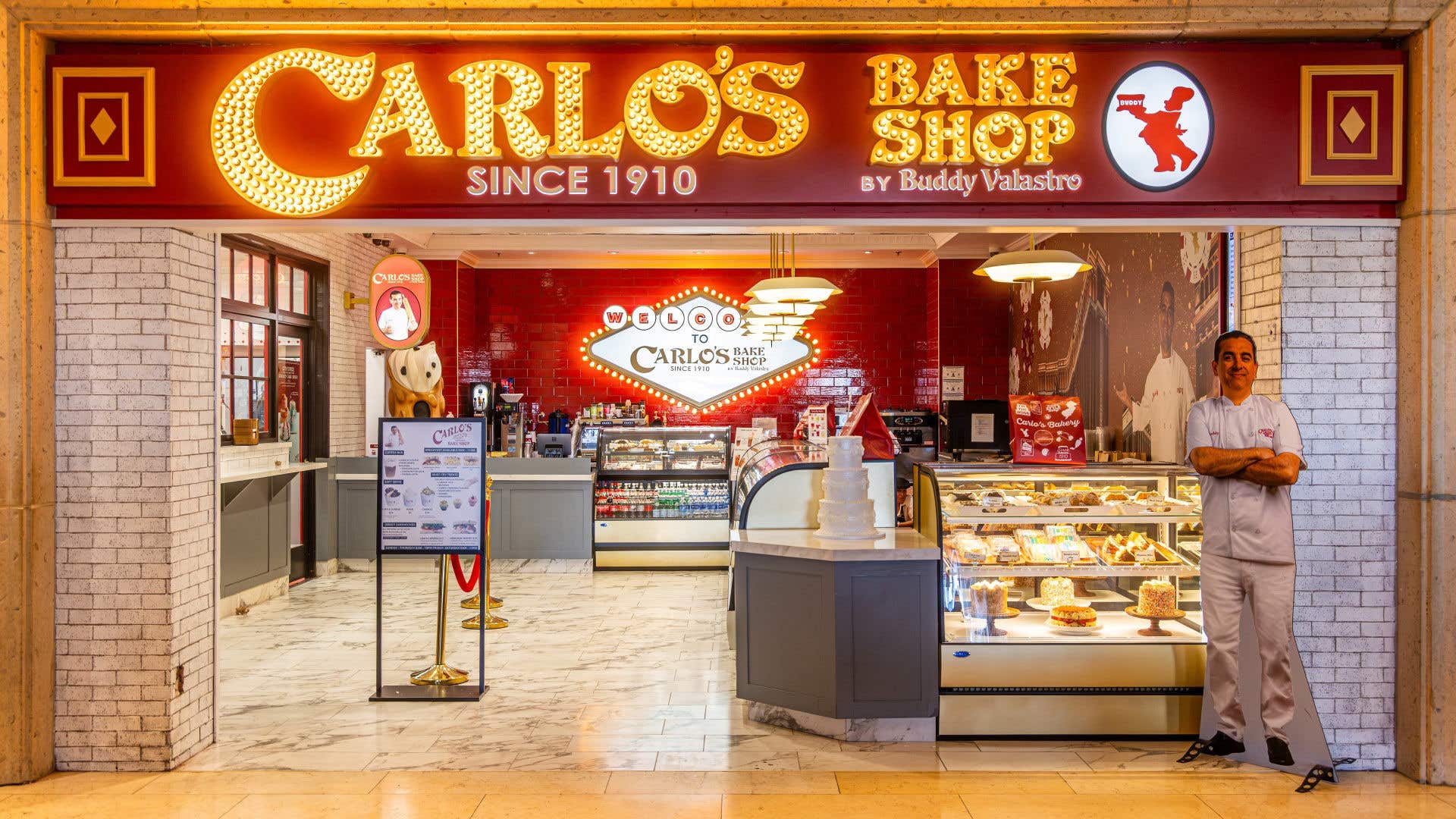 Carlo’s Bake Shop entrance with glowing sign, display counters, and baked goods.