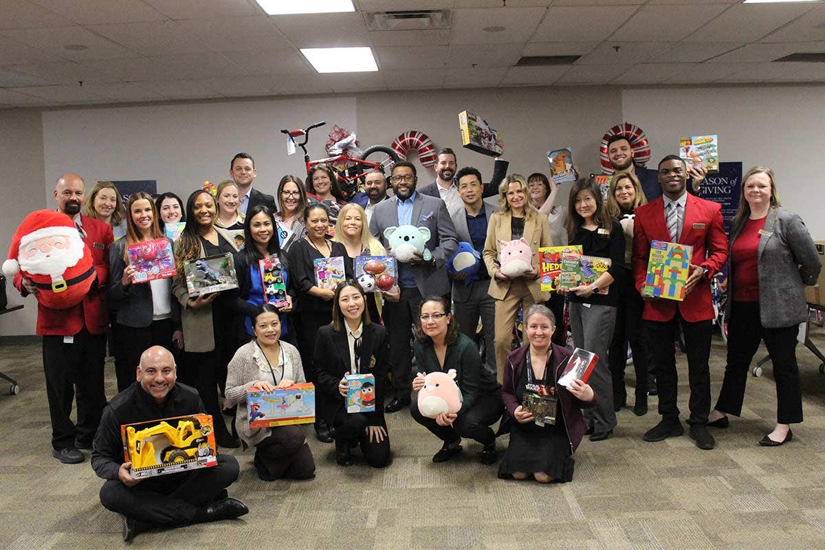A group of people smiling and holding various toys while posing for a group photo indoors.