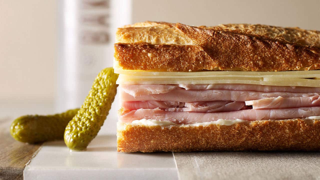 A classic ham and cheese baguette sandwich from Bouchon Bakery, served with two small pickles on the side