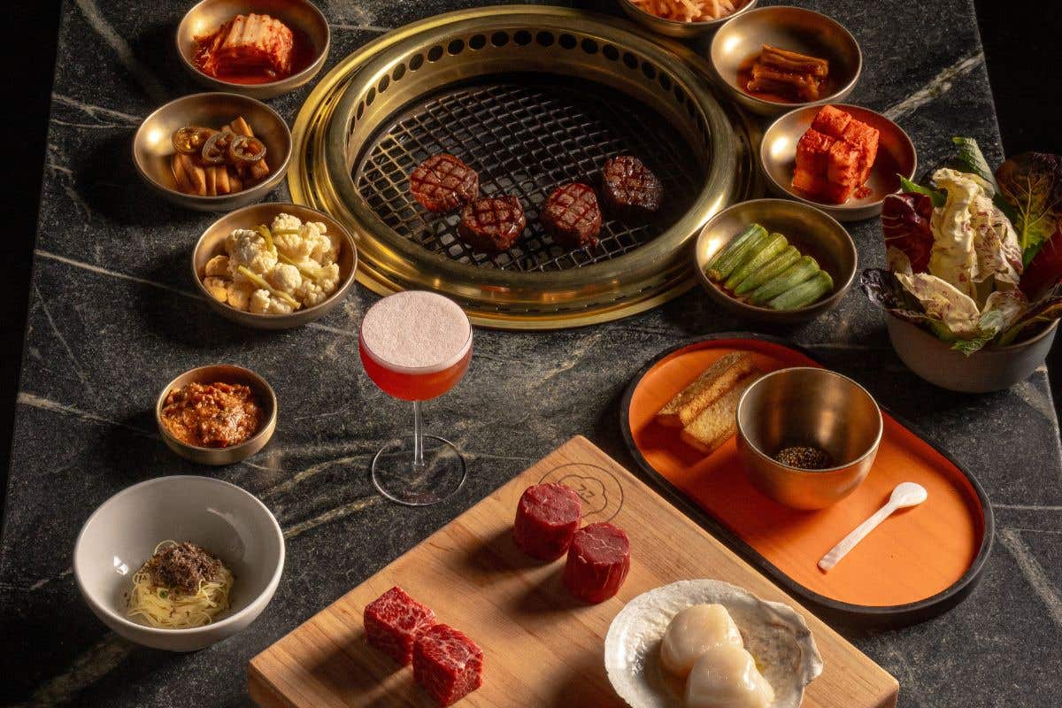 Korean BBQ setup with grilled meat, banchan, and raw cuts on a board.