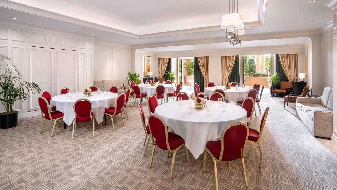 A large, elegantly decorated lounge with round tables, red chairs, and a chandelier.