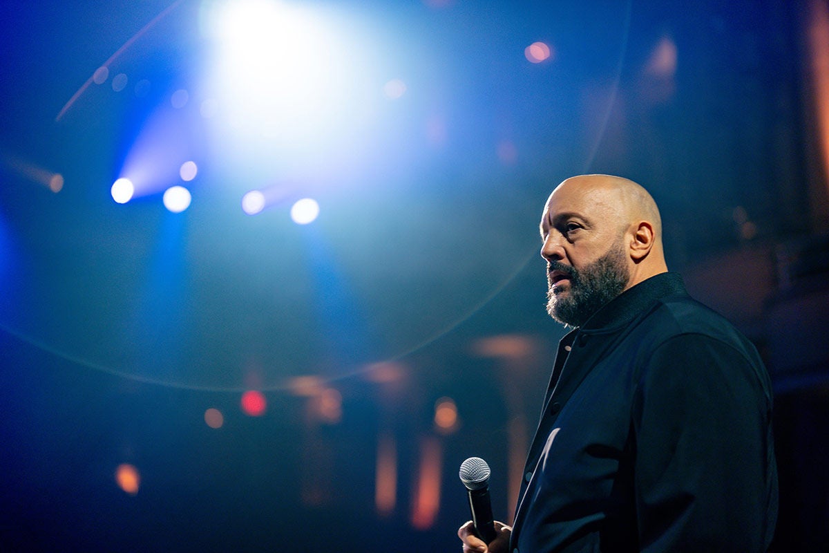 Comedian Kevin James on stage holding a microphone.
