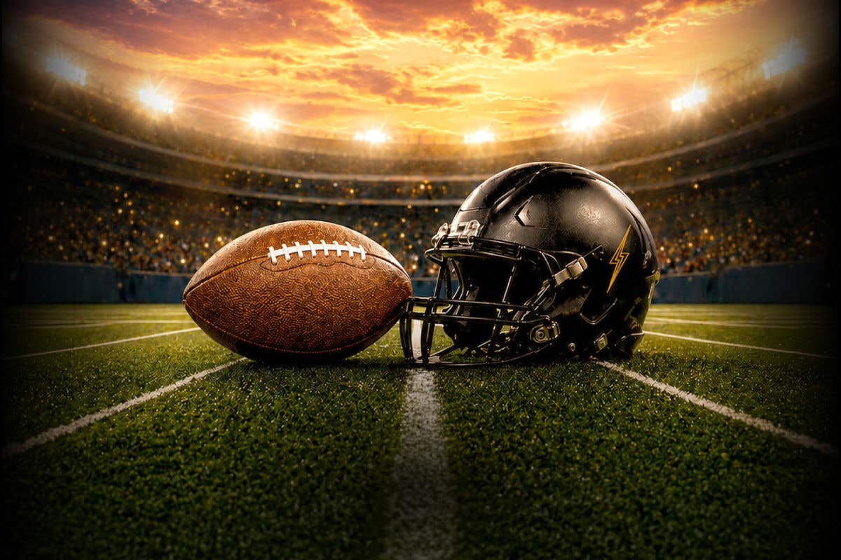 Brown football and black football helmet resting on a football field at midfield, with stadium lights and a glowing sunset sky in the background.