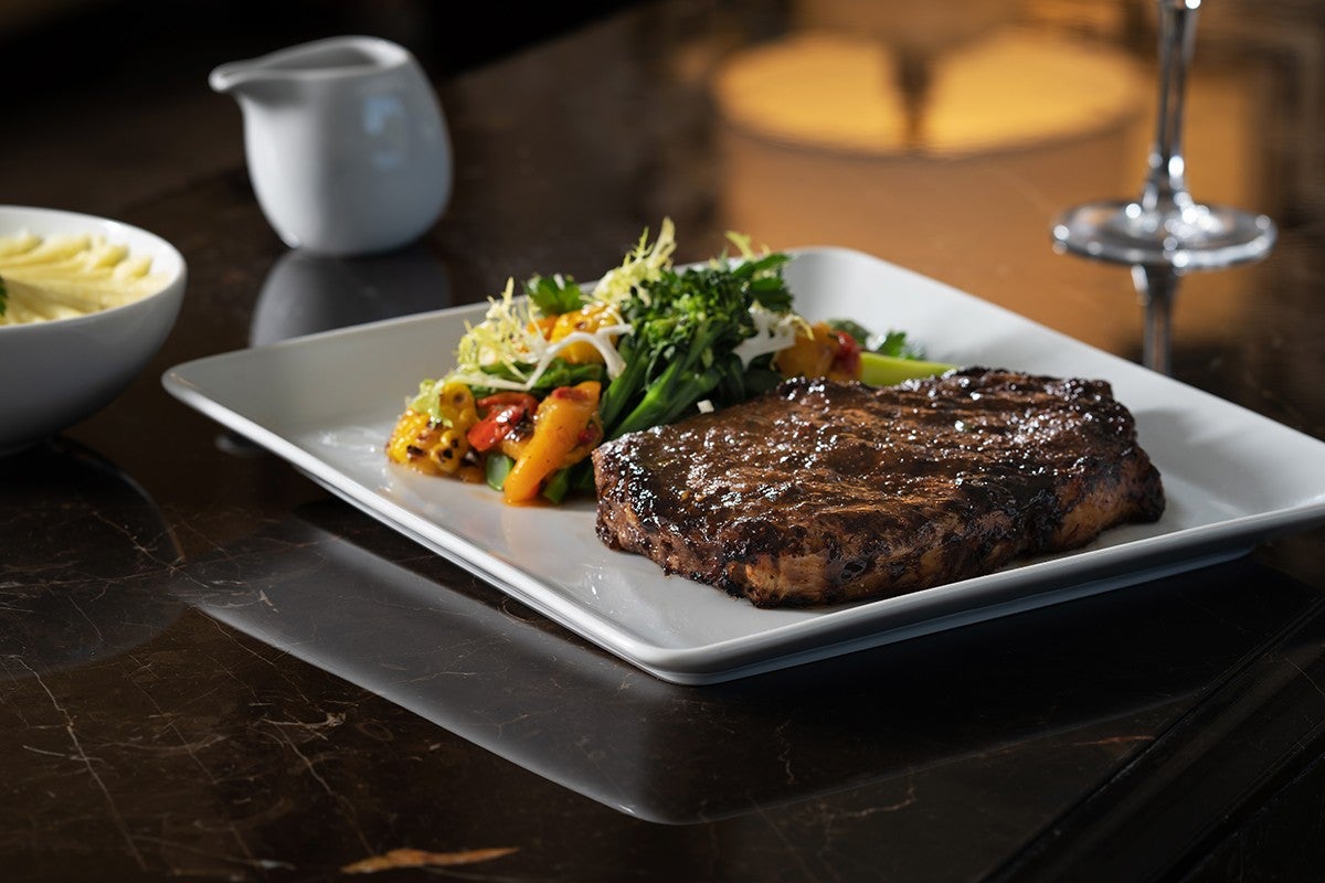 A grilled steak with vegetables and a wine glass on a table.