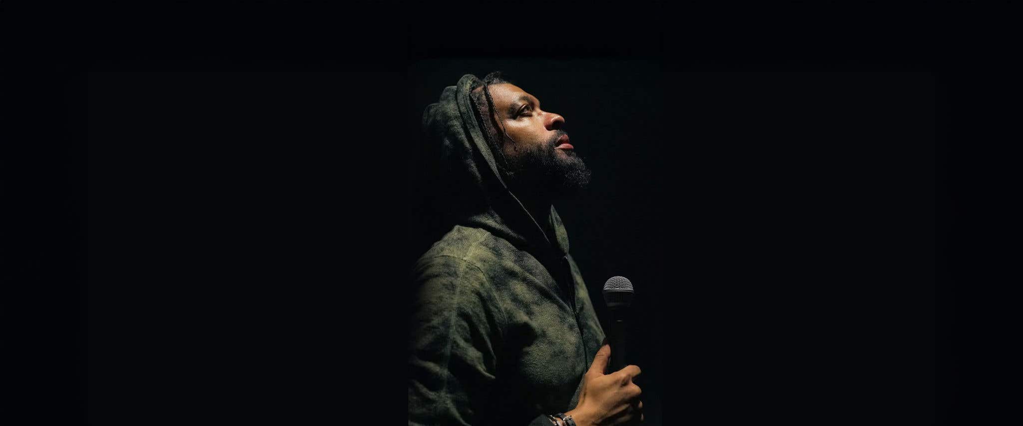 DeRay Davis wearing a varsity jacket standing on a brick road looking off into the distance.