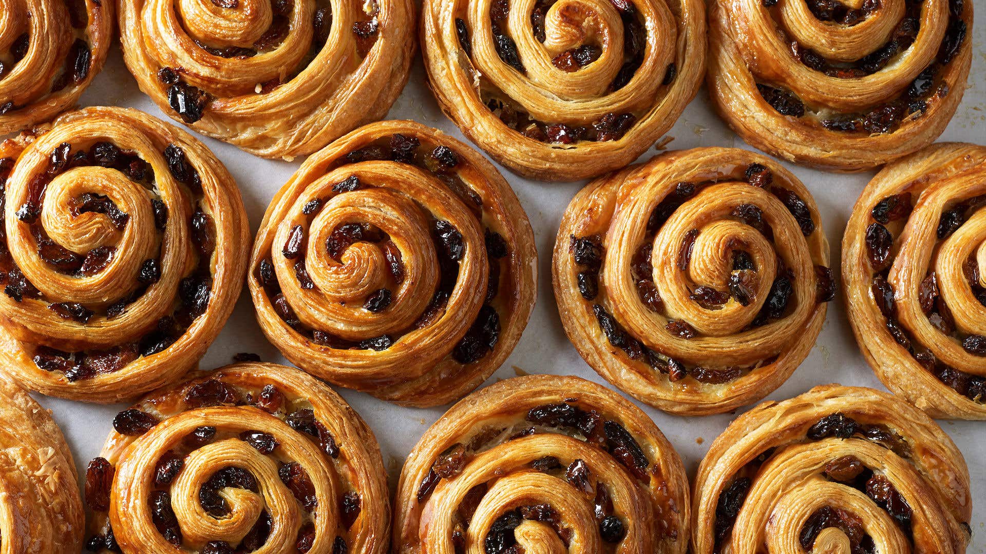 An overhead shot of freshly baked Pain aux Raisins arranged on a baking sheet.