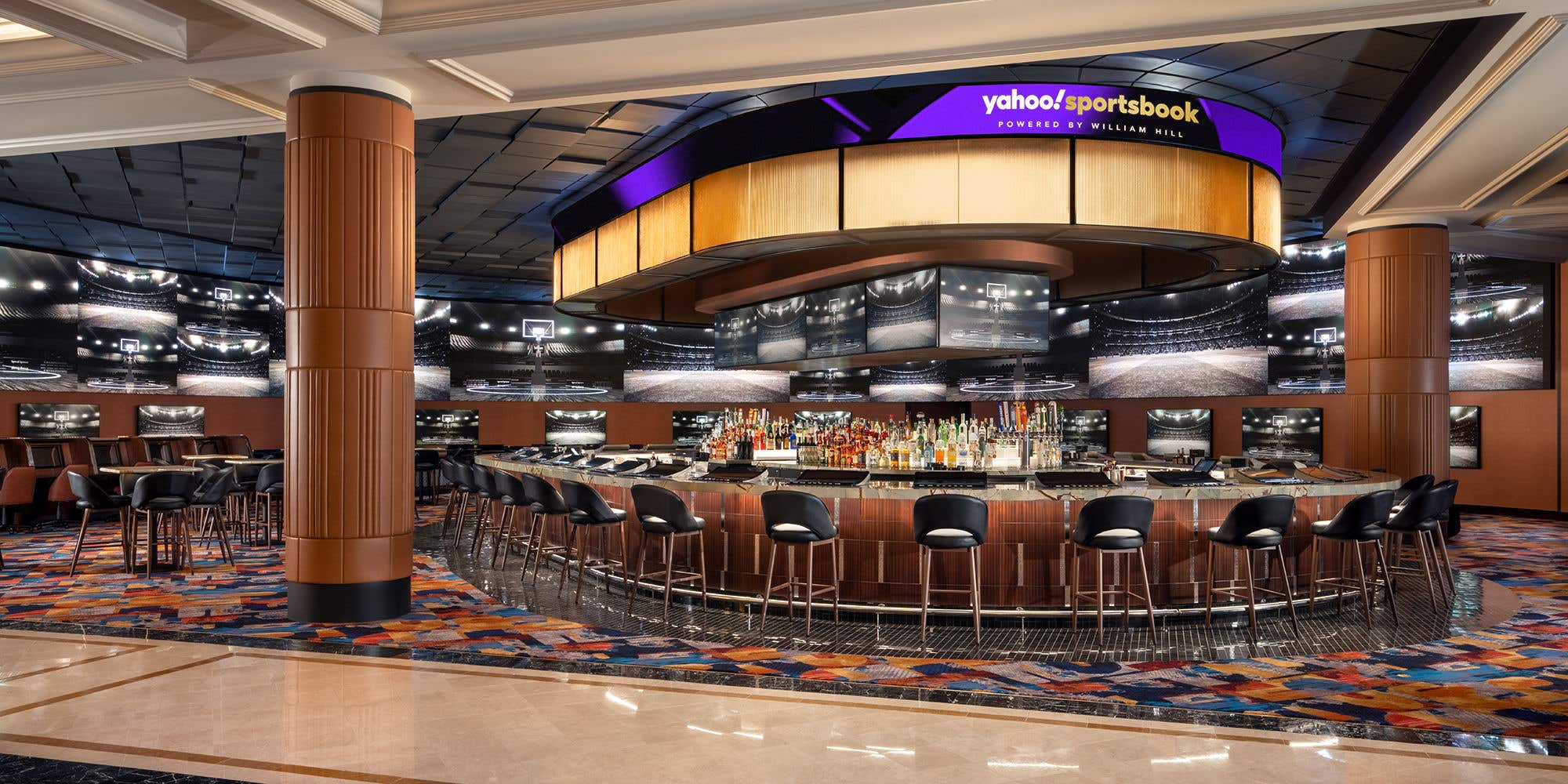 Yahoo Sportsbook with a central circular bar, surrounded by high-backed stools, and featuring multiple screens showing basketball courts.