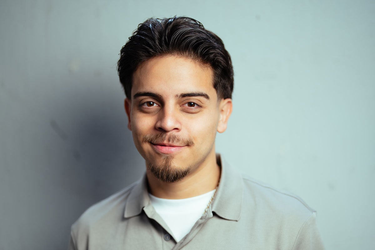 Ralph Barbosa with short dark hair and a light gray shirt smiles in front of a light blue background.
