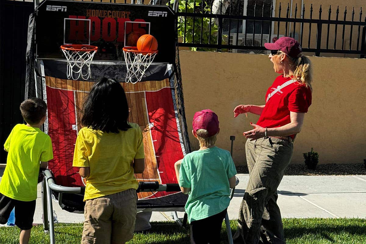 Kids play basketball outdoors cheered on by a smiling volunteer.