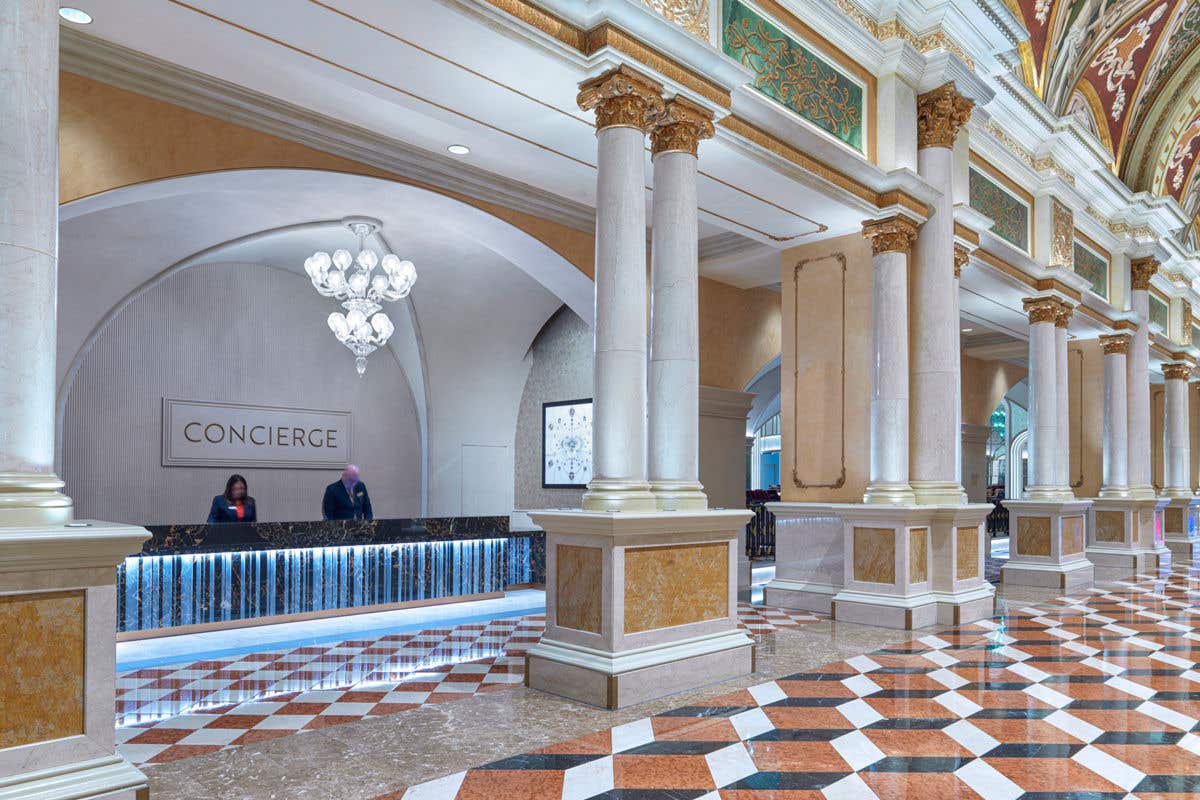 A hotel foyer with a concierge desk on the left with two people.
