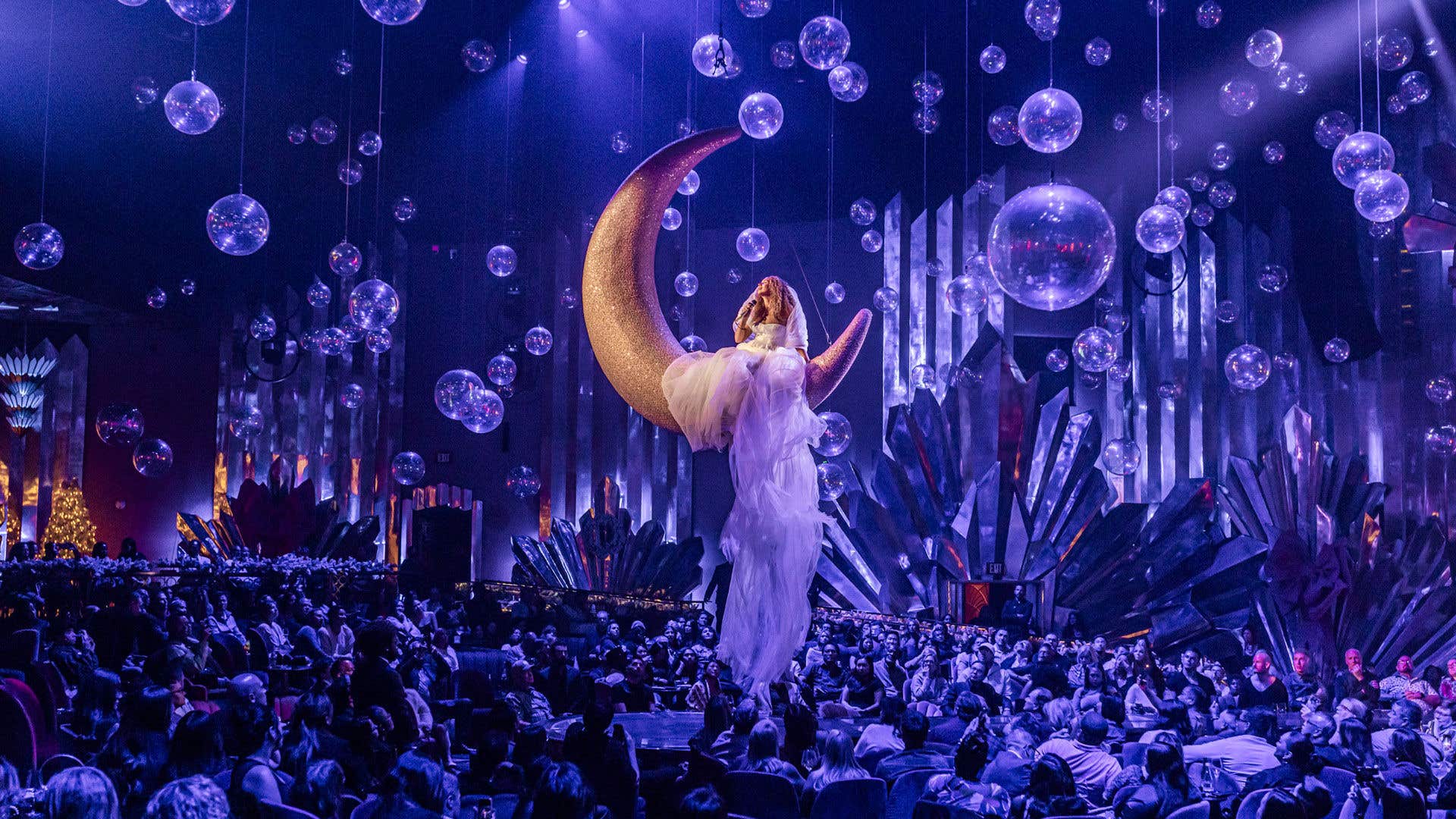 Leona Lewis on a moon in a flowing white dress suspended in the air with the audience staring up at her. 
