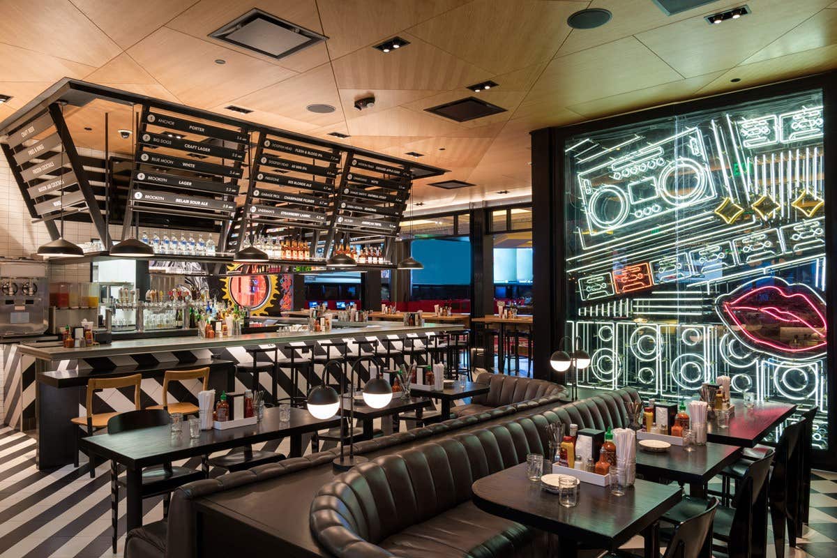 Modern restaurant with neon light wall art, a central bar, and black leather seating.