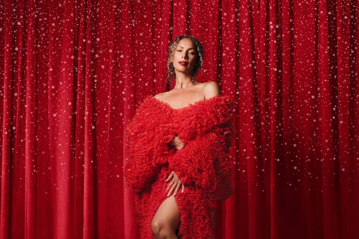 Leona Lewis in red dress in front of red curtain background with snow falling all around her. 