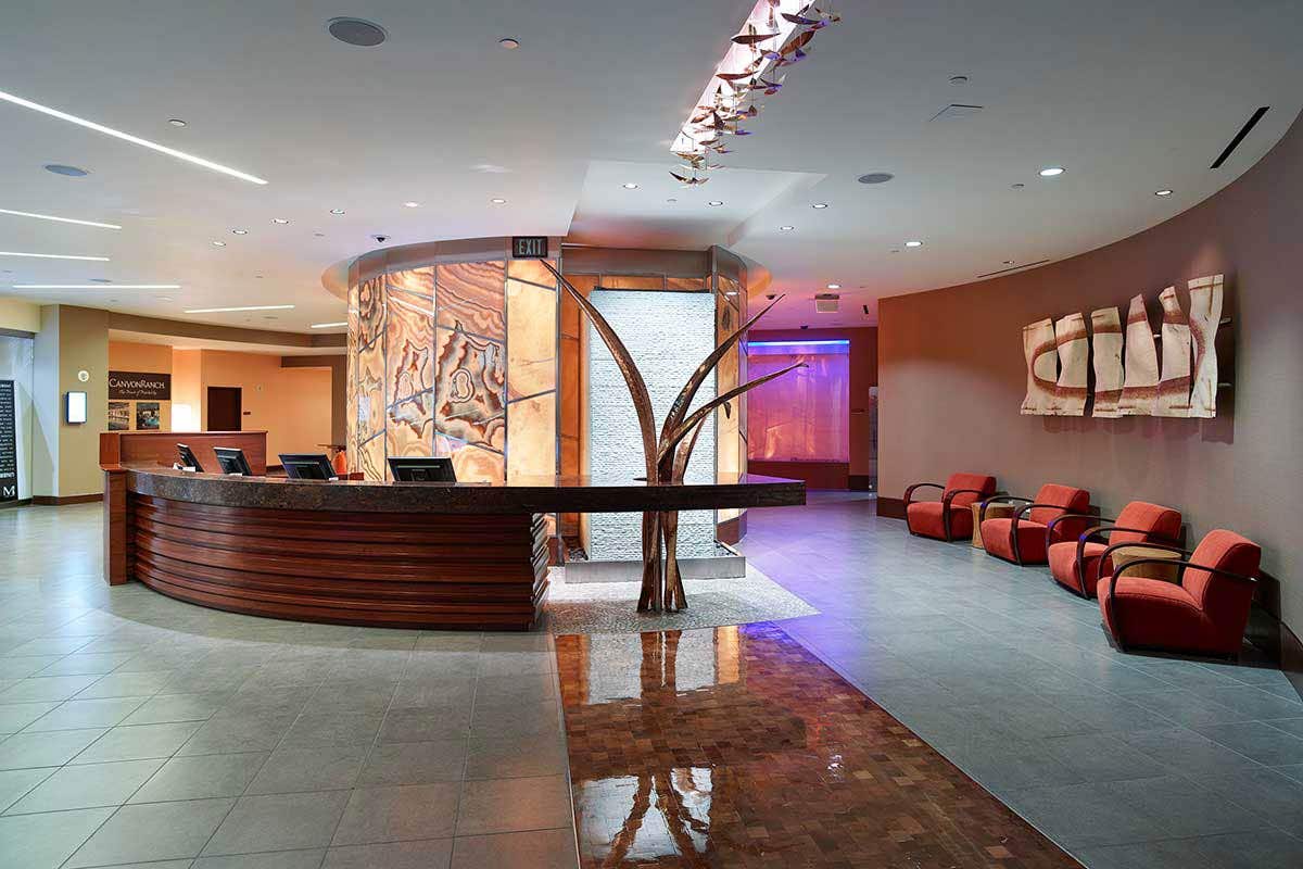 A curved check-in desk with a bronze metal tree sculpture next to it and a row of armchairs.