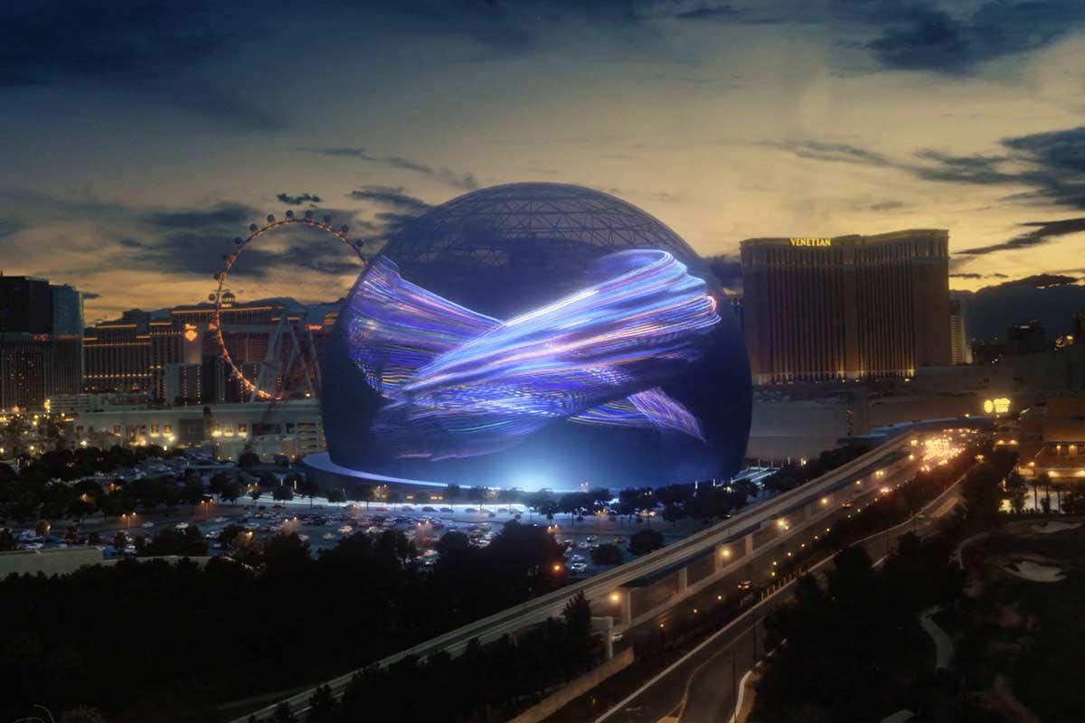 A large, illuminated spherical building with dynamic light patterns at dusk, with a Ferris wheel and cityscape in the background.
