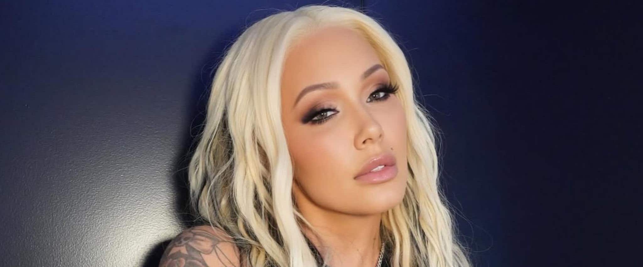 Bunnie Xo in black top standing in front of black background looking at the camera. 