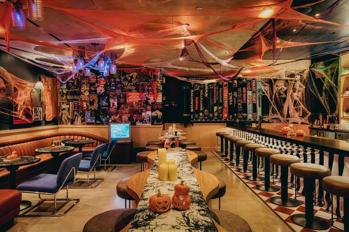 Halloween-themed bar decorated with cobwebs, pumpkins, candles, and vintage horror movie posters.