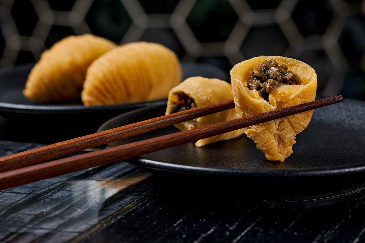 Close-up of golden-brown pastries on black plates with chopsticks, against a dark background.