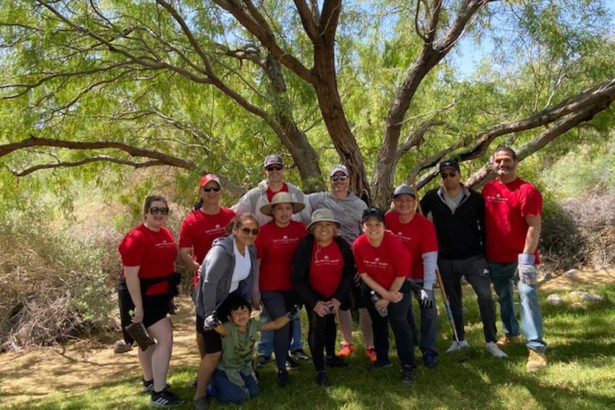 A group of volunteers cleaning trails outdoors, posing happily under sunny blue skies.
