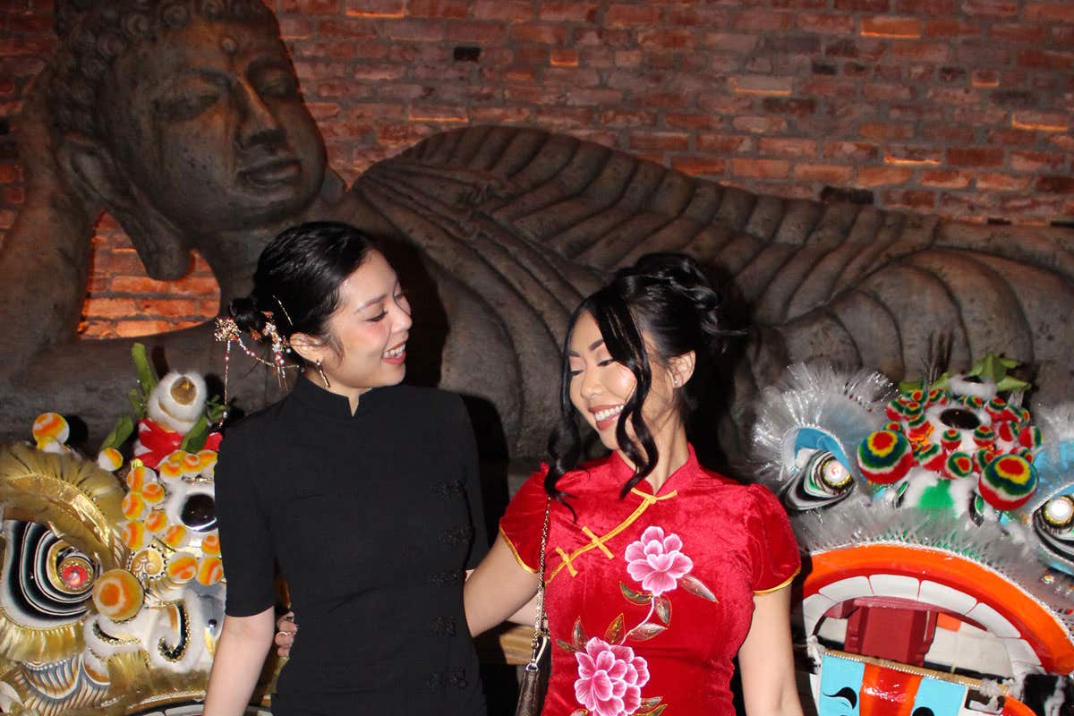 Two women dressed in traditional Chinese outfits smiling in front of two lions used for lion dance. 