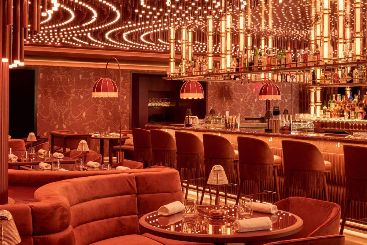 Warm, upscale lounge bar with plush seating, glowing amber lighting, and a mirrored bar lined with bottles.
