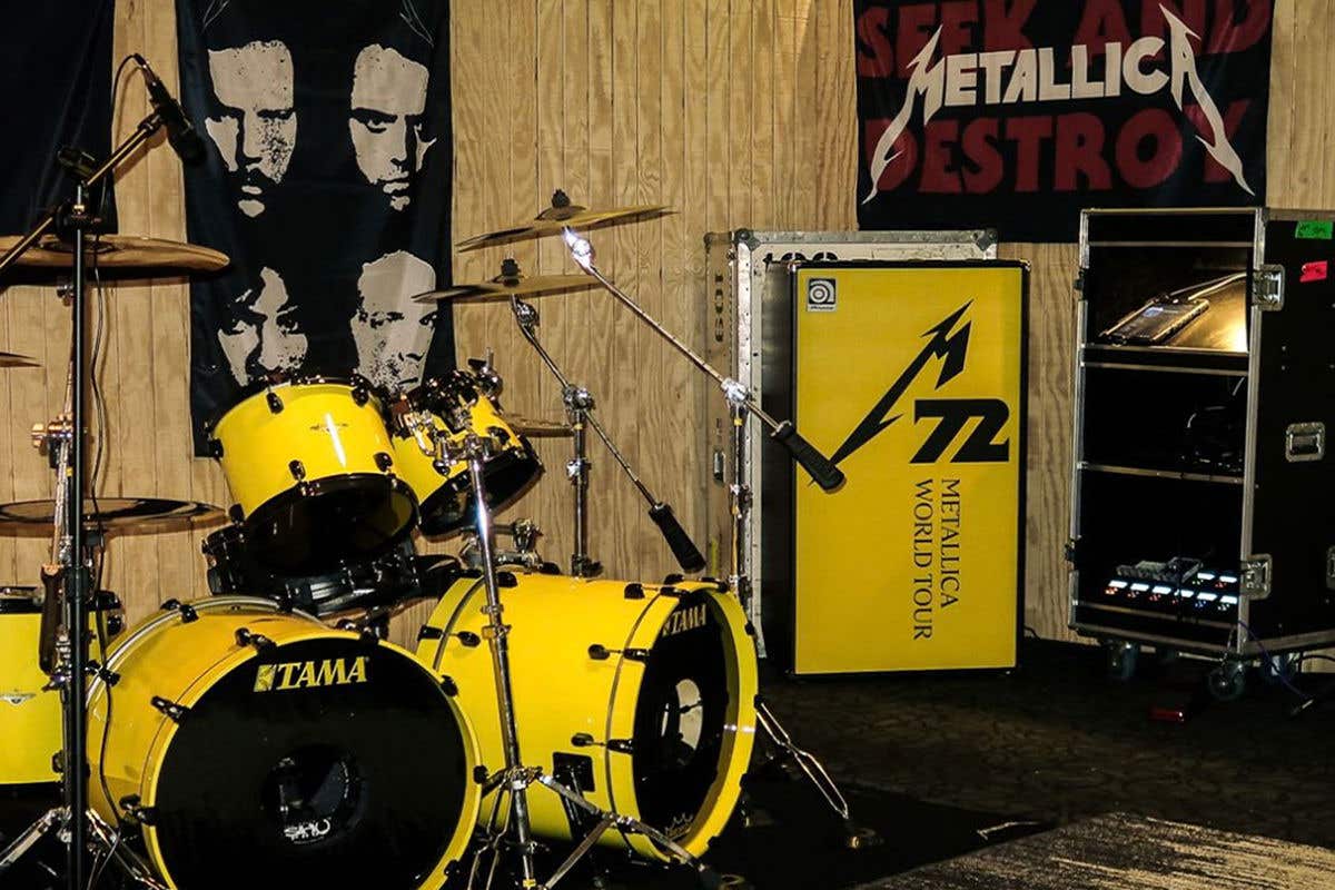 A yellow drum kit with Metallica flags behind it.
