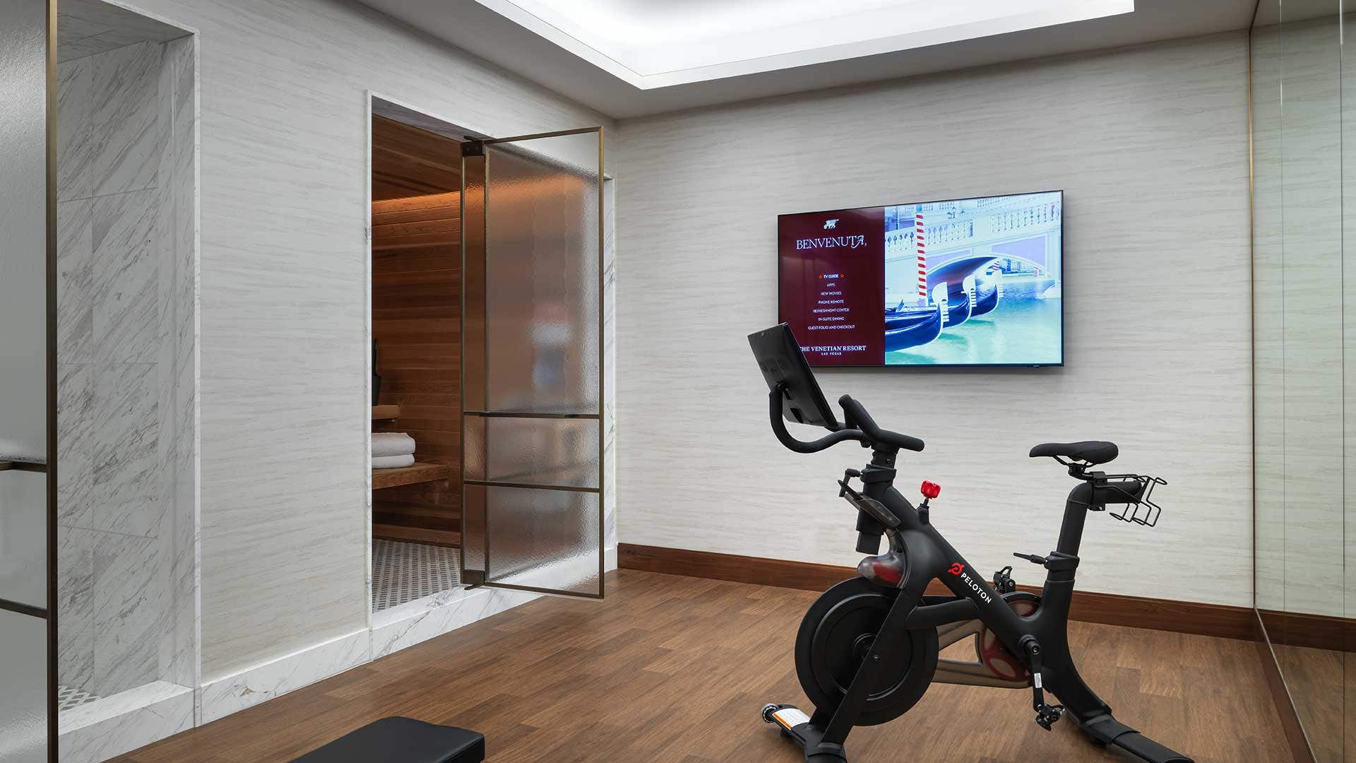 A private workout room with hardwood floors, a mirrored wall, TV, exercise bike, a sauna room, and a steam room.