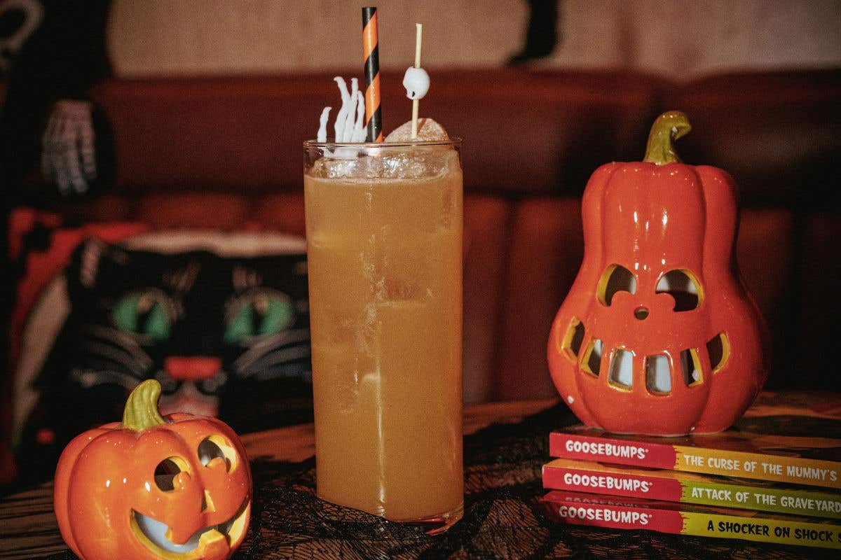 Halloween cocktail garnished with a skull pick, surrounded by pumpkin decorations and spooky books.