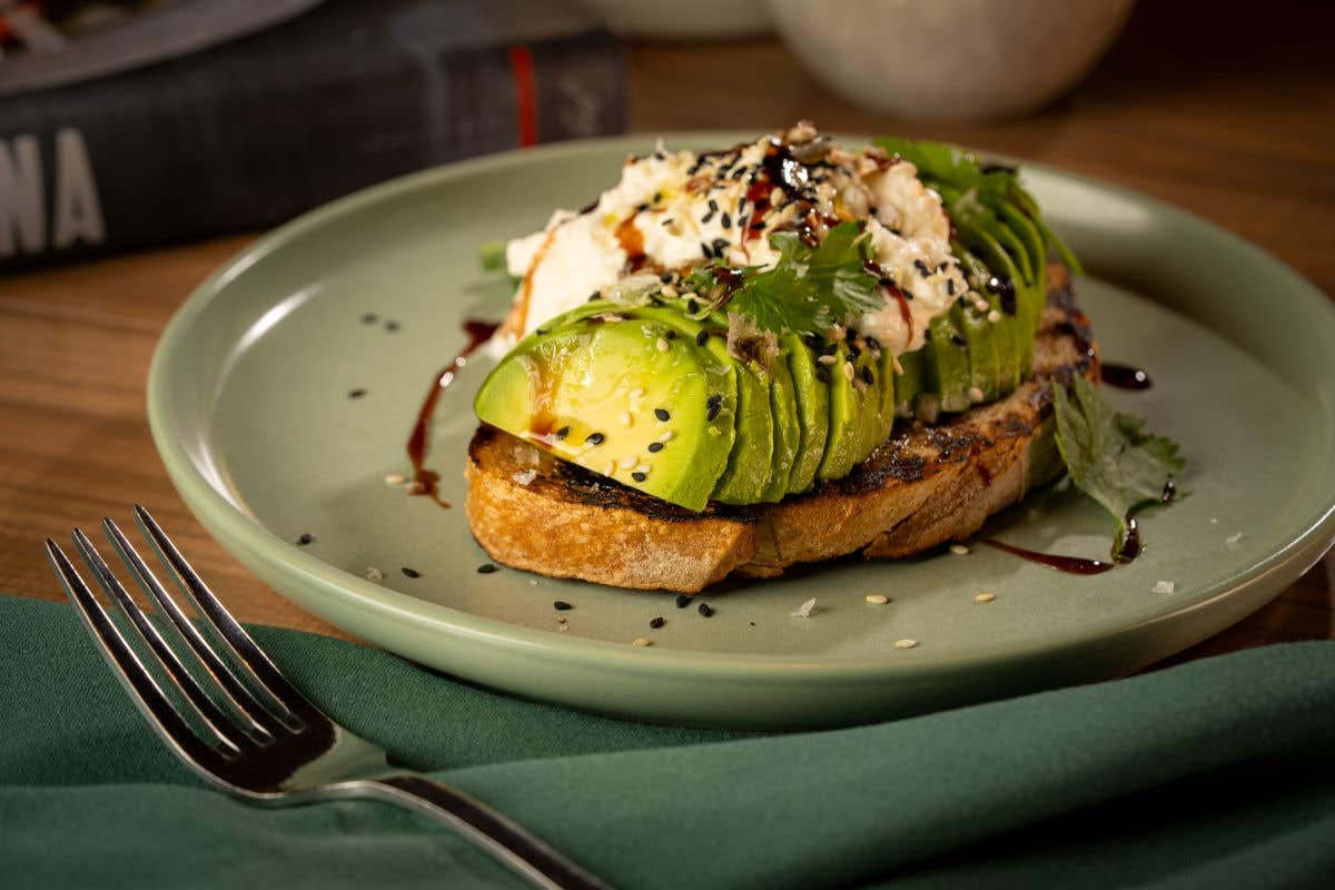 Avocado toast topped with sliced avocado, sesame seeds, and herbs.