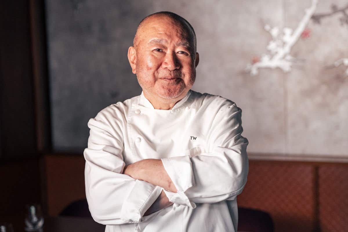 Chef Wakuda in a white coat standing with arms crossed in a restaurant setting.