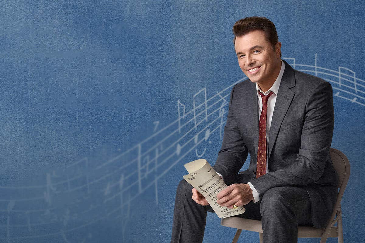 Actor and singer Seth MacFarlane sitting on a folding chair, set against a blue background with music notes.