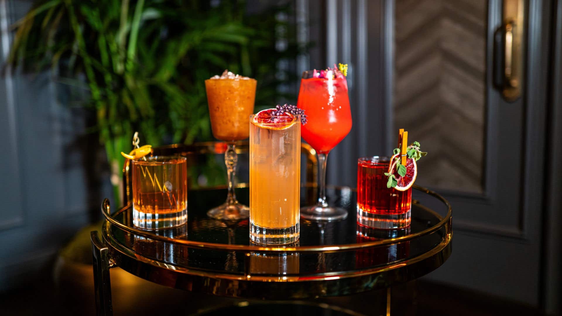 Assortment of colorful craft cocktails served on a round bar cart.