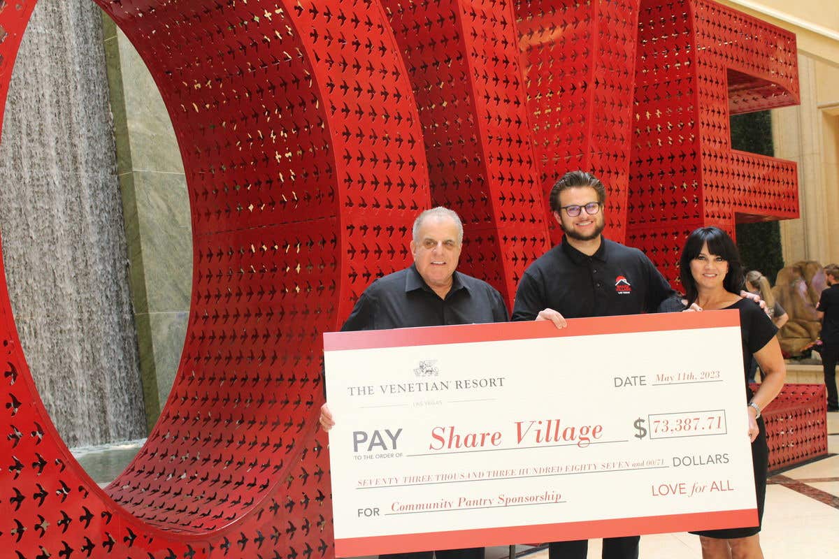 Share Village participants holding a large check for the organization in front of the LOVE sign.