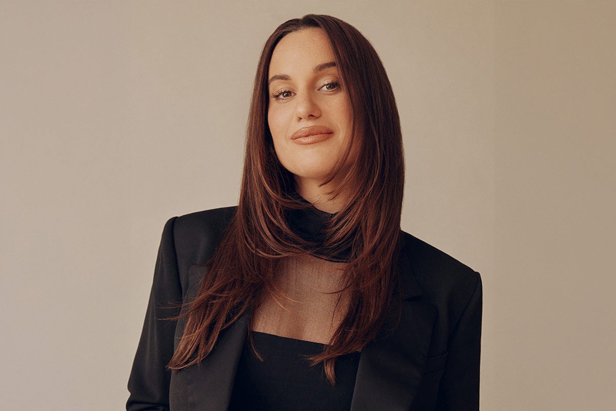 Comedian Hannah Berner, wearing a black blazer set against a gold background.