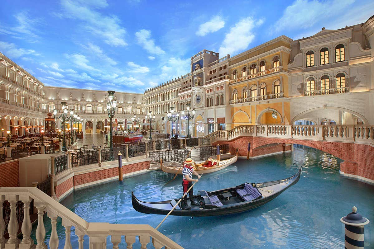 Indoor canal with gondolas and Venetian-style buildings under a painted sky ceiling.