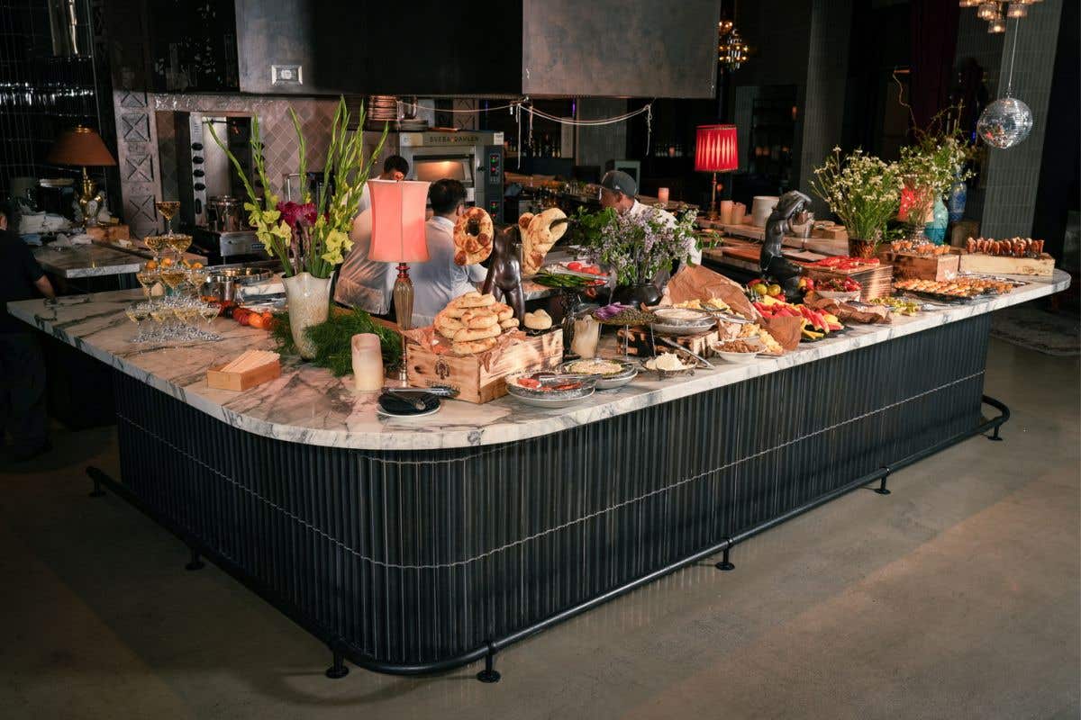 Large marble-topped buffet with breads, appetizers, and floral arrangements in a modern restaurant space.