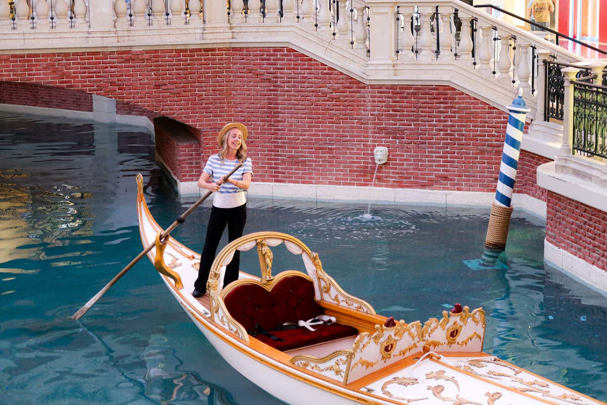 Woman in blue and white striped shirt and black pants standing on top of white gondola that is floating in the water.