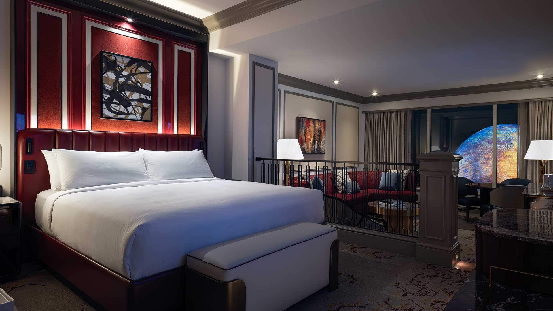 A hotel room at night with a king bed on the left, a living room area on the right, and a view of the Sphere through window on the right.
